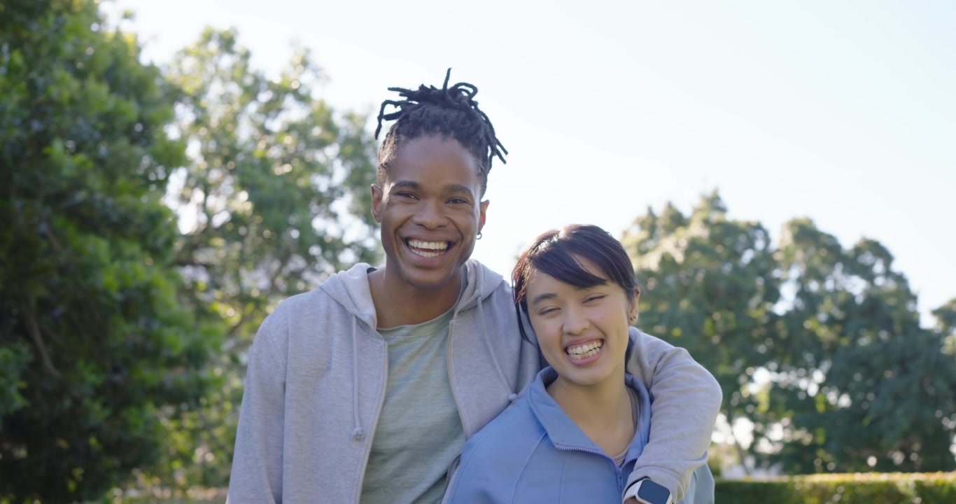 Diverse couple greeting, talking, embracing and posing on park lawn with yoga mat before class