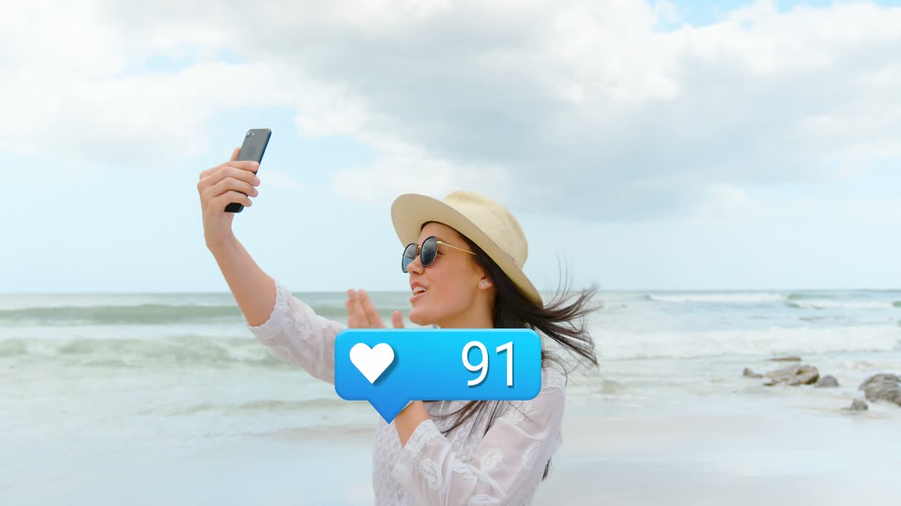 Animasi hati dan reaksi media sosial di atas wanita Kaukasia bahagia yang sedang berfoto di pantai.