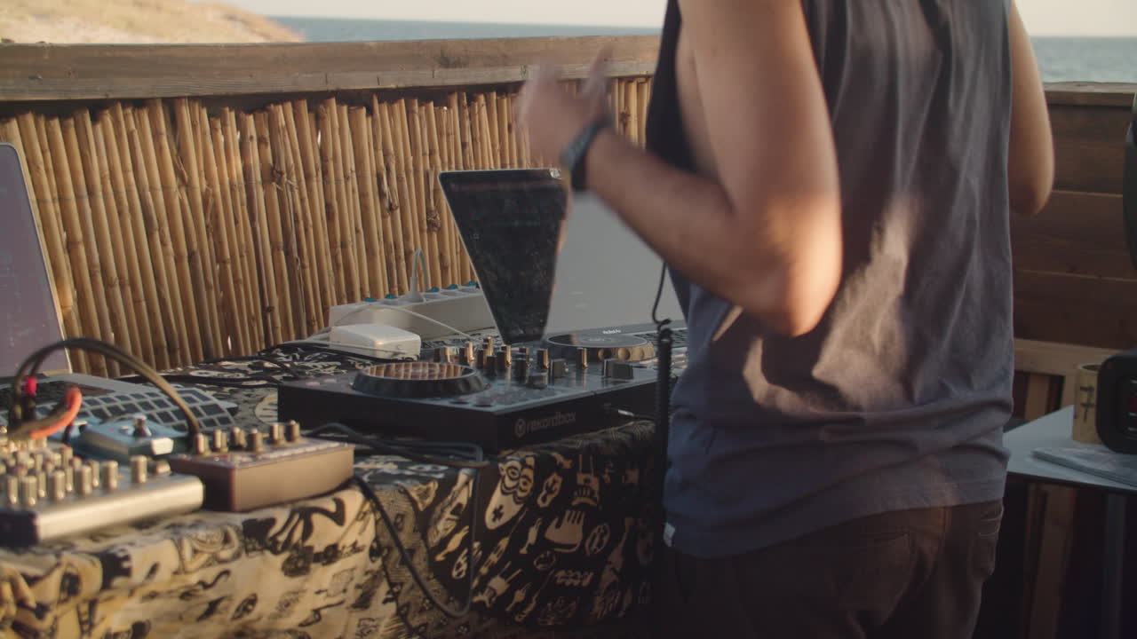 Closeup of Dj hands adjusting mixer controller desk in exotic summertime location, sunset, zoom out