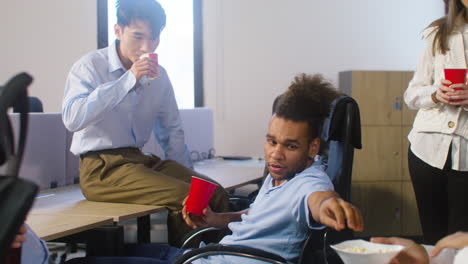 hombre comiendo palomitas de maíz y hablando con un colega en la fiesta de la oficina