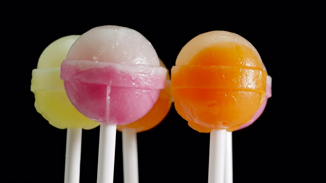 dulces de los niños piruletas. una gran cantidad de dulces de colores están girando en un fondo negro. dulces en un palo blanco