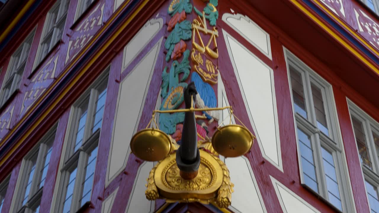 Insegna decorativa a forma di bilancia dorata su una storica facciata a graticcio presso il Museo Stoltze nel centro storico di Francoforte, con dettagliati elementi architettonici.