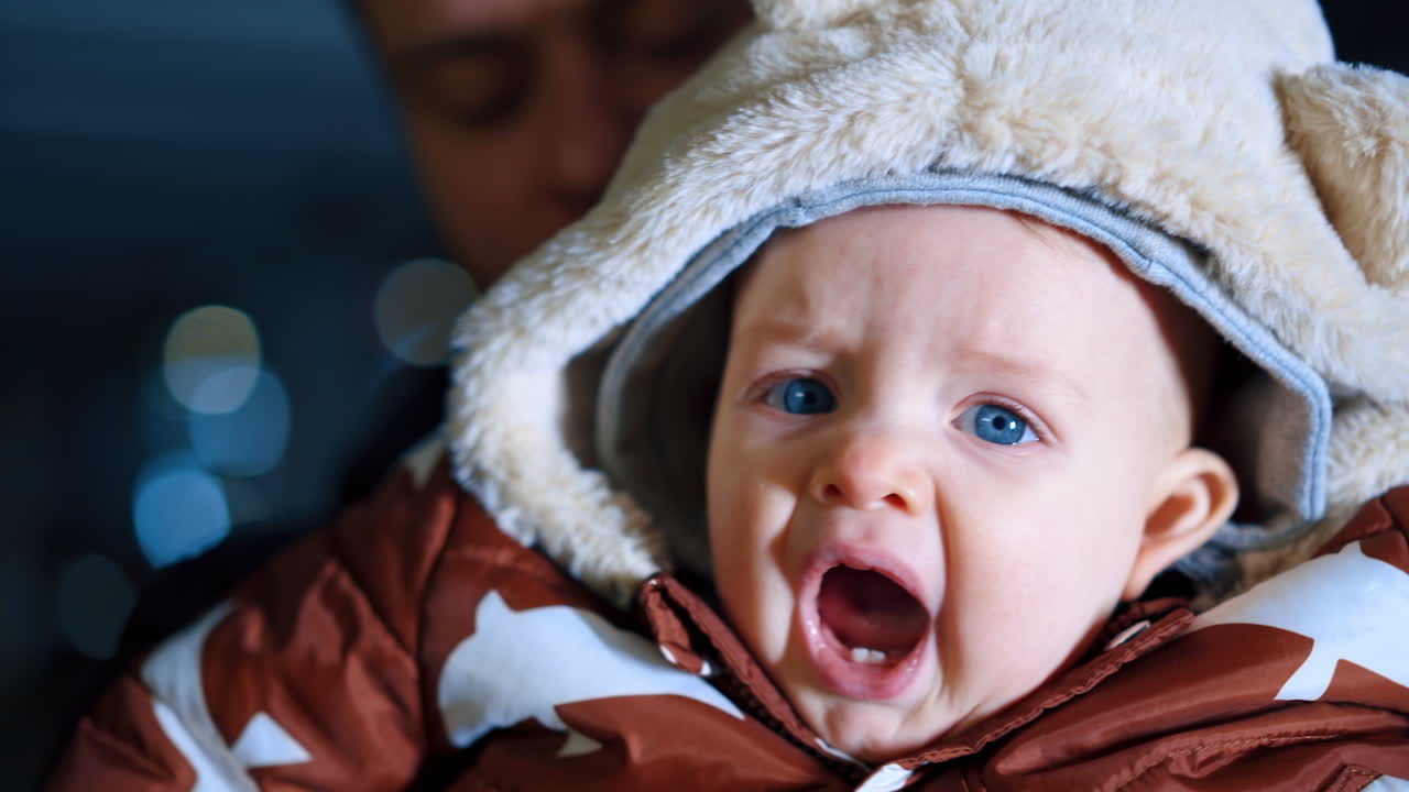 Cute blue-eyed Caucasian baby in a warm jacket with hood. Close up portrait on a lovely child with two front teeth.