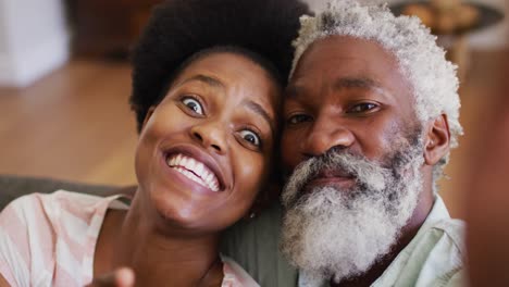 Glückliches-Afroamerikanisches-Paar,-Das-Sich-Auf-Der-Couch-Entspannt-Und-Lächelnd-Und-Winkend-Einen-Videoanruf-Macht