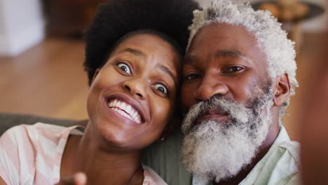 Happy-african-american-couple-relaxing-on-couch-making-video-call-smiling-and-waving