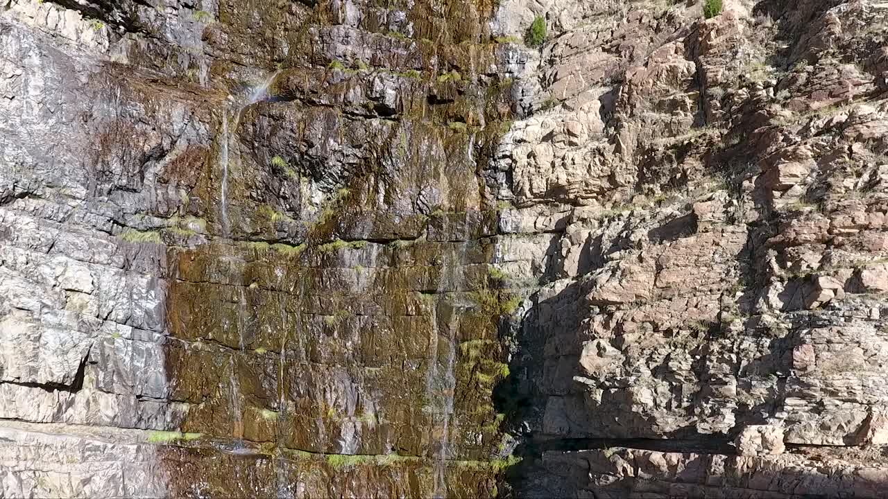 una pequeña cascada en el cañón ogden, utah, se filtra por rocas escarpadas como lo ve un dron ascendente desde muy cerca