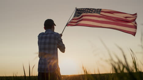 silhouette of a young man waving the american flag. standing in a field of wheat at sunset