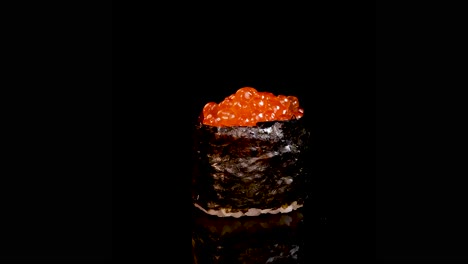 a single piece of salmon roe sushi rotates smoothly under dramatic lighting, highlighting vibrant orange fish eggs and glossy seaweed against a black backdrop