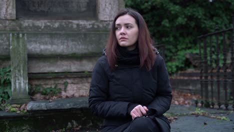 sad young woman sitting alone in the cemetery on a cold day