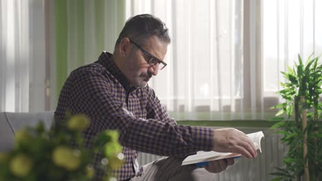 Un-Hombre-Maduro-Con-Gafas-Está-Leyendo-Un-Libro-En-Casa.