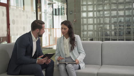 a young businessman with beard and suit has a business meeting with a pretty young businesswoman on the sofas in the common area of the office building 3