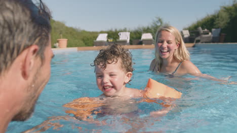 parents teaching son to swim on summer vacation in outdoor swimming pool with inflatable armbands