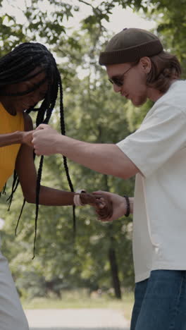 two young adults engaged in a playful interaction, holding hands outdoors in a park setting.