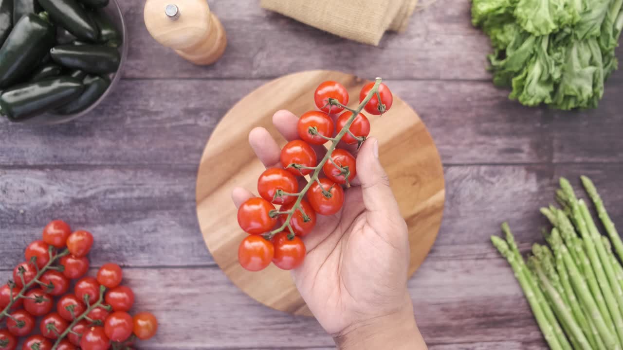 나무 절단 보드 에 체리 토마토 한 어리 를 들고 있는 손