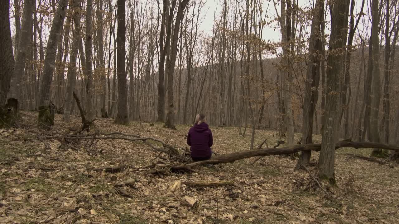 겨울에 루마니아 호이아 바치우 숲에 있는 쓰러진 나무에 배낭을 메고 보라색 재킷을 입은 여성