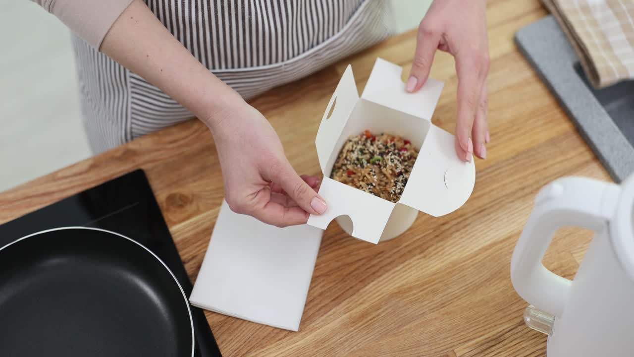 Mani che aprono una scatola da asporto di noodles asiatici in una cucina
