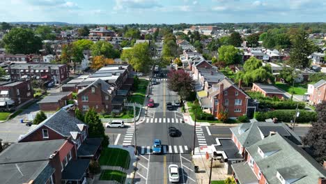 aerial view of a suburban neighborhood with brick houses, tree-lined streets, and cars driving along a main road on a clear day