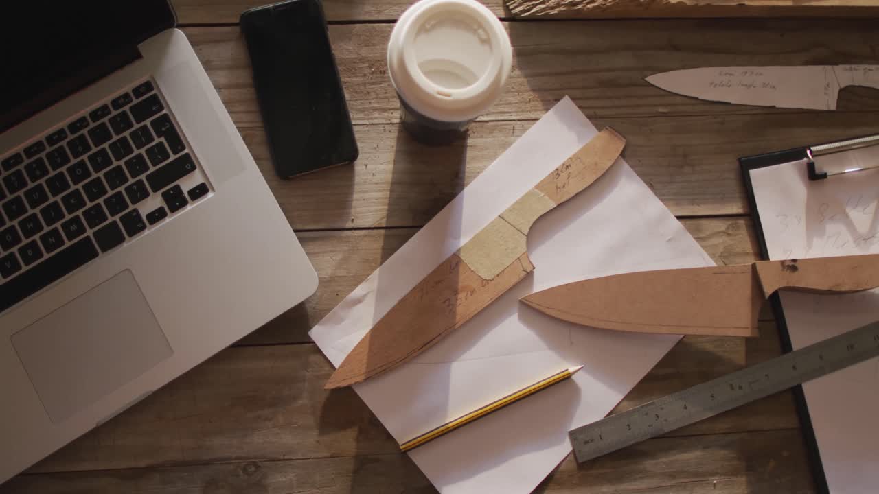 tableta, teléfono inteligente, cuchillos de madera y papeles sobre el escritorio en el taller del fabricante de cuchillos