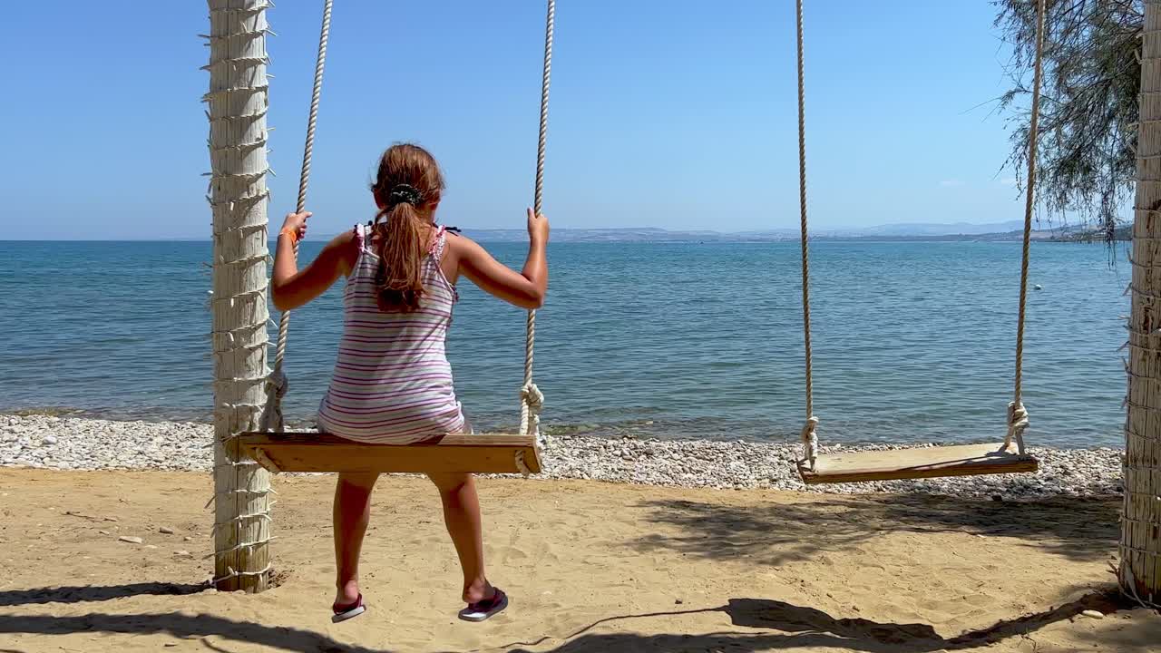 niña pelirroja en vacaciones de verano disfruta balanceándose en un columpio de cuerda mirando el mar en calma