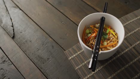 composition of bowl of pad thai with chopsticks on wooden background