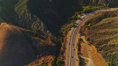 freeway in the mountainous locality on sunny bright day. descending drone footage over the road with moving cars. aerial view.