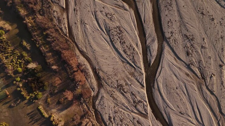 Cinematic top-down drone view of the Wanaka riverbed at sunset, highlighting the patterns of the dry river and flowing water in the Otago Region, New Zealand