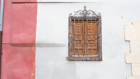 an architectural detail of a traditional house, featuring a window with wooden shutters protected by a classic, ornate wrought-iron grille in cuenca, spain.