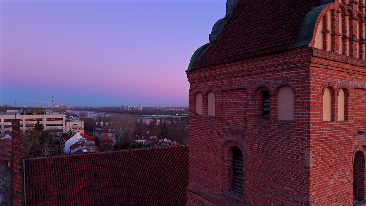 el dron orbita justo a través de la torre de ladrillo iluminada por el sol de la iglesia de santa maría en varsovia, polonia, un punto de referencia gótico histórico en la hora azul.