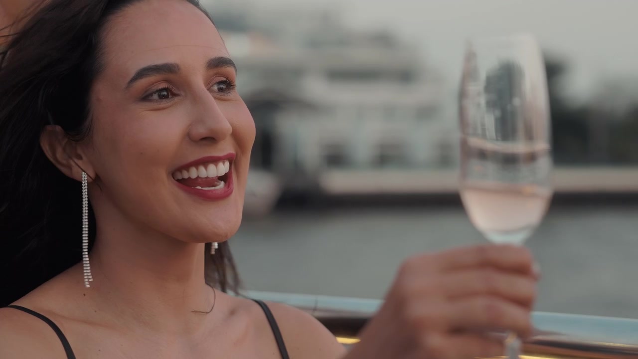Giovane donna elegante che sorride e sorseggia vino all'aperto