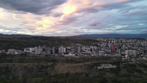fotografía aérea de la puesta de sol en tbilisi, georgia. edificios rodeados de montañas.