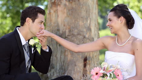 Happy-newlyweds-sitting-in-the-park-beside-a-tree