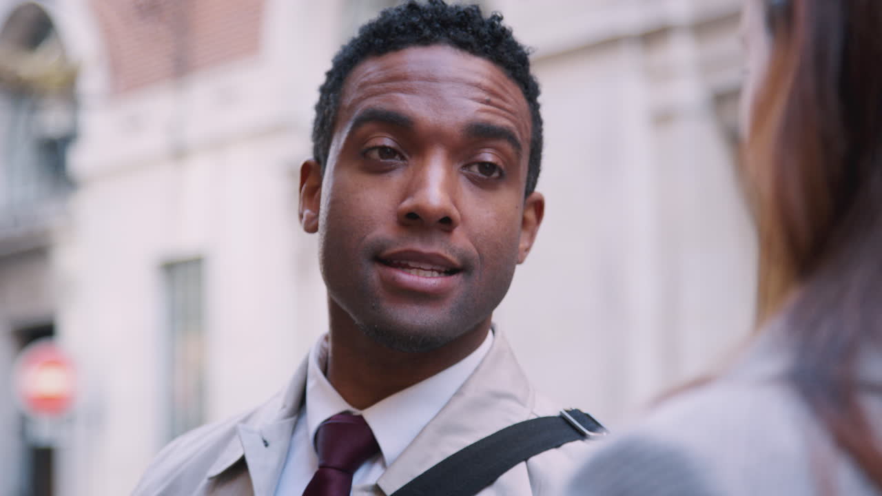 Millennial black businessman standing in the street talking with his white female colleague, close up, selective focus