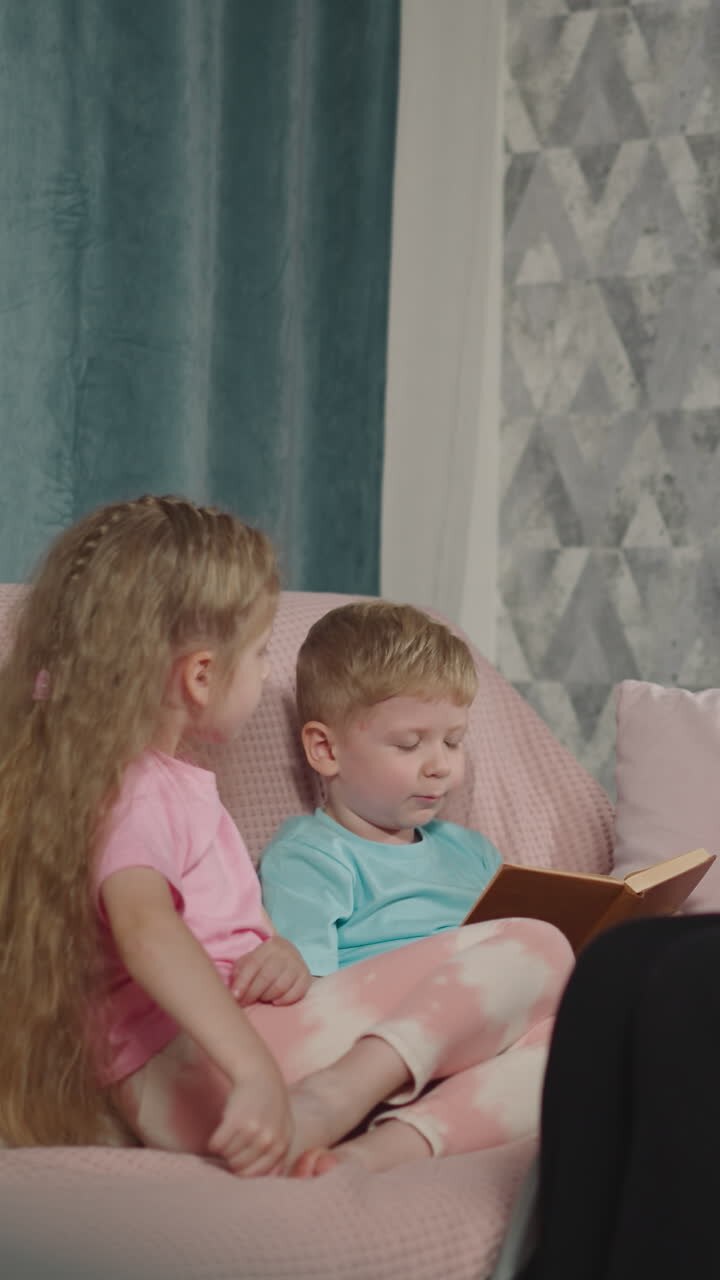 Attentive mother in wheelchair and sister listen to blond boy reading book nodding head. Woman with muscular dystrophy spends evening with kids in flat
