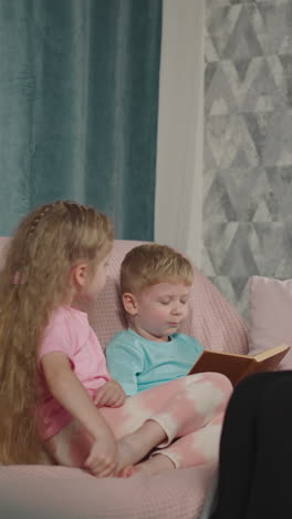 attentive mother in wheelchair and sister listen to blond boy reading book nodding head. woman with muscular dystrophy spends evening with kids in flat