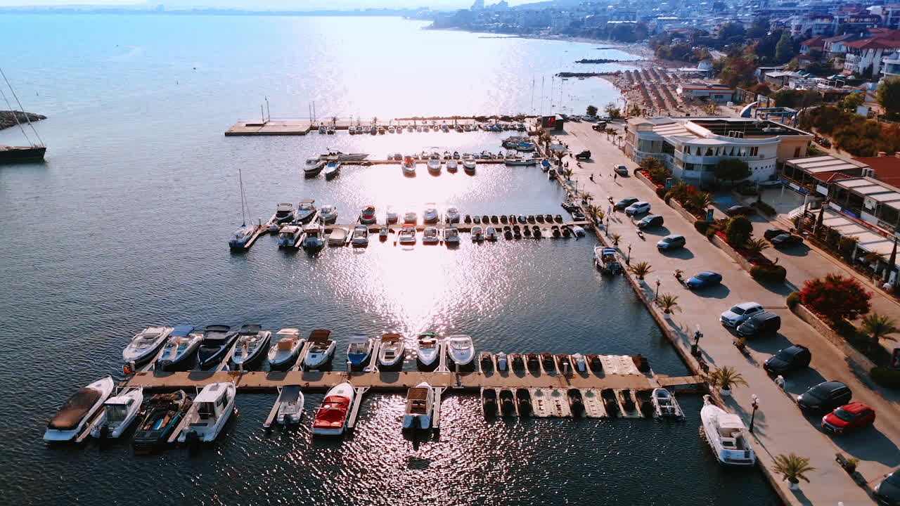 Boats docked at a marina during daytime. Many boats are anchored at a busy marina, surrounded by a vibrant promenade and a calm shimmering sea