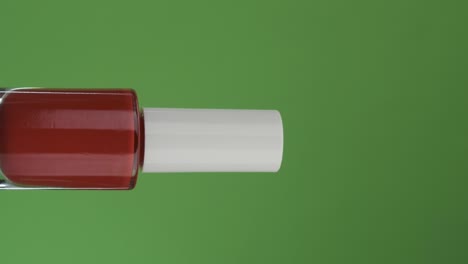 horizontal rotation of a glass bottle with nail polish, on a green screen. close-up.