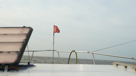 small fishing boat with a red flag on the front sails on rough seas on a gloomy overcast day