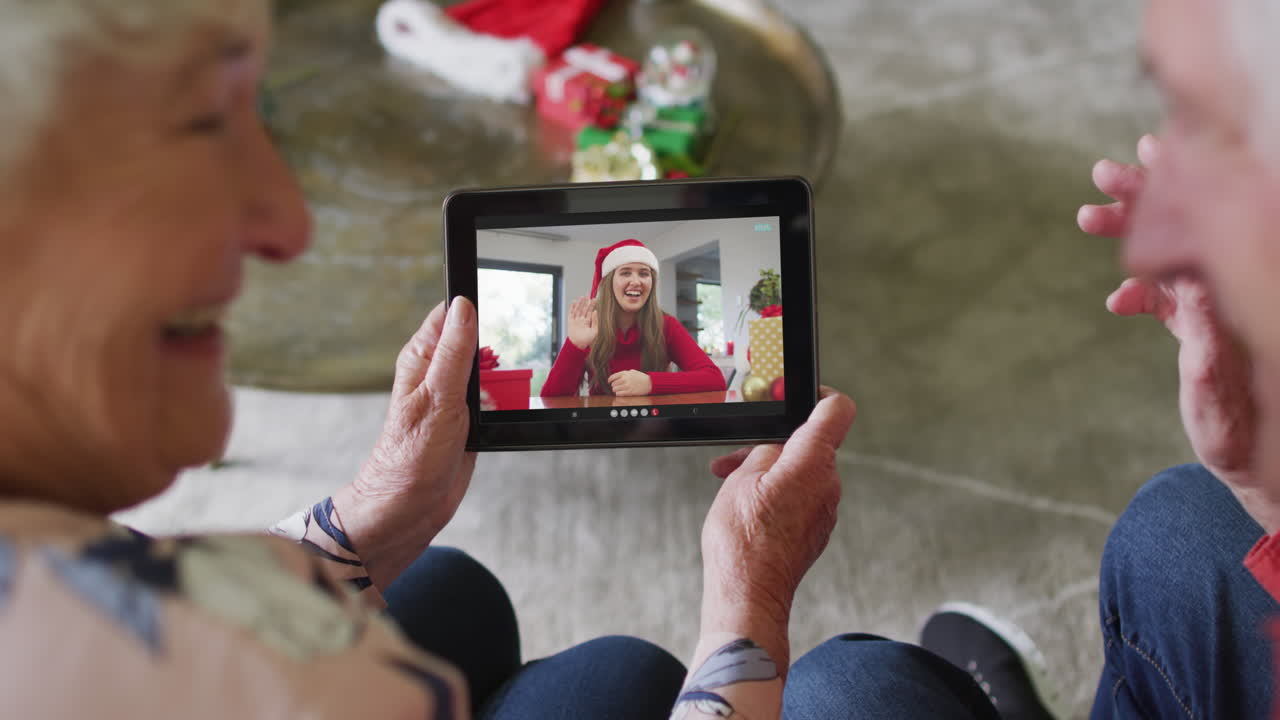 Coppia anziana caucasica che usa un tablet per una videochiamata di Natale con una donna sorridente sullo schermo