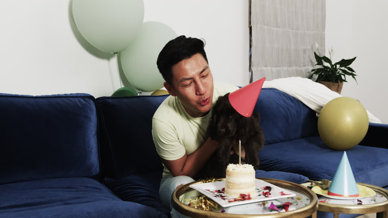 Celebrating at home, Asian man holding dog with party hat and cake