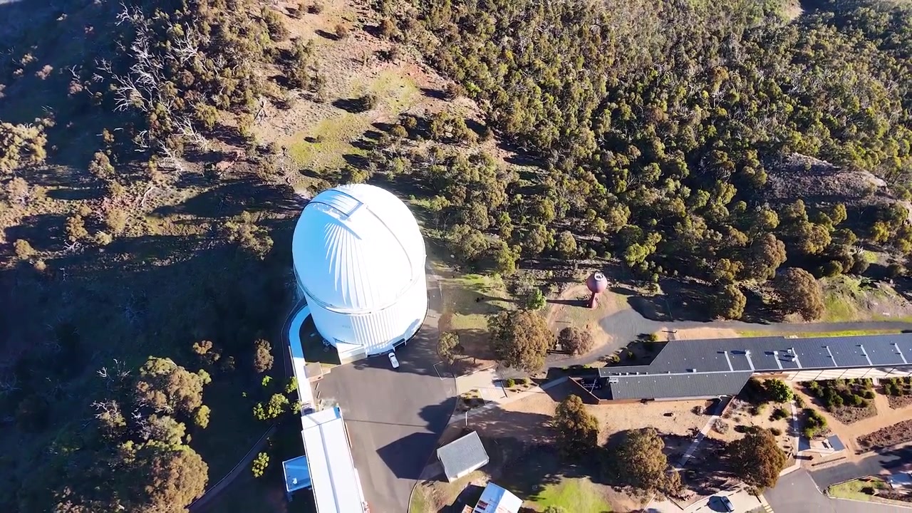 Toma aérea de gran angular de una cúpula de telescopio blanca en el Observatorio Siding Spring, Australia.