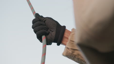 close up of person wearing black dotted glove gripping colorful safety rope outdoors with sky in background showing action, strength, and precision during physical task