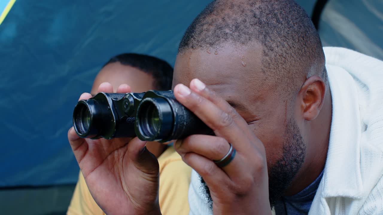 African American father and son laughing, father raising black binoculars tent opening son watching