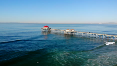 Wide,-slow-aerial-4k-drone-move-in-to-Huntington-Beach-Pier-with-diner-visible,-Pacific-Ocean,-California,-morning,-sunny