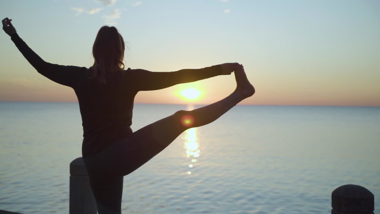 Woman extending leg into standing yoga pose at sunrise. Slow Motion.