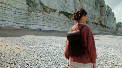 mujer con mochila en una playa de guijarros junto al océano