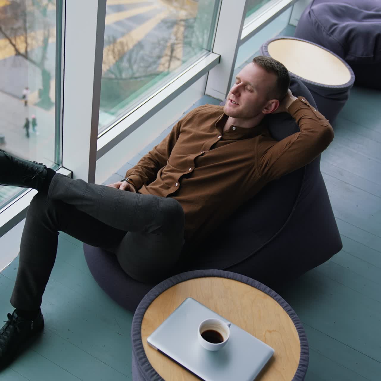 Businessman relaxing in office. Young man sitting in comfortable armchair with closed eyes and dreaming at daytime next to the window with city view. Top view