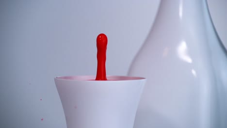 la gota roja cae lentamente en una taza blanca.
