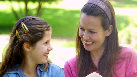 madre e hija leyendo juntos en un banco del parque