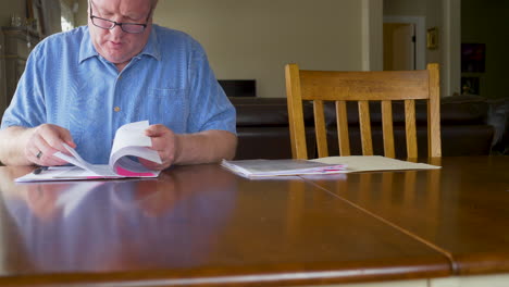 a mature man at a table looking through tax, loan or other documents with concern - sliding reveal