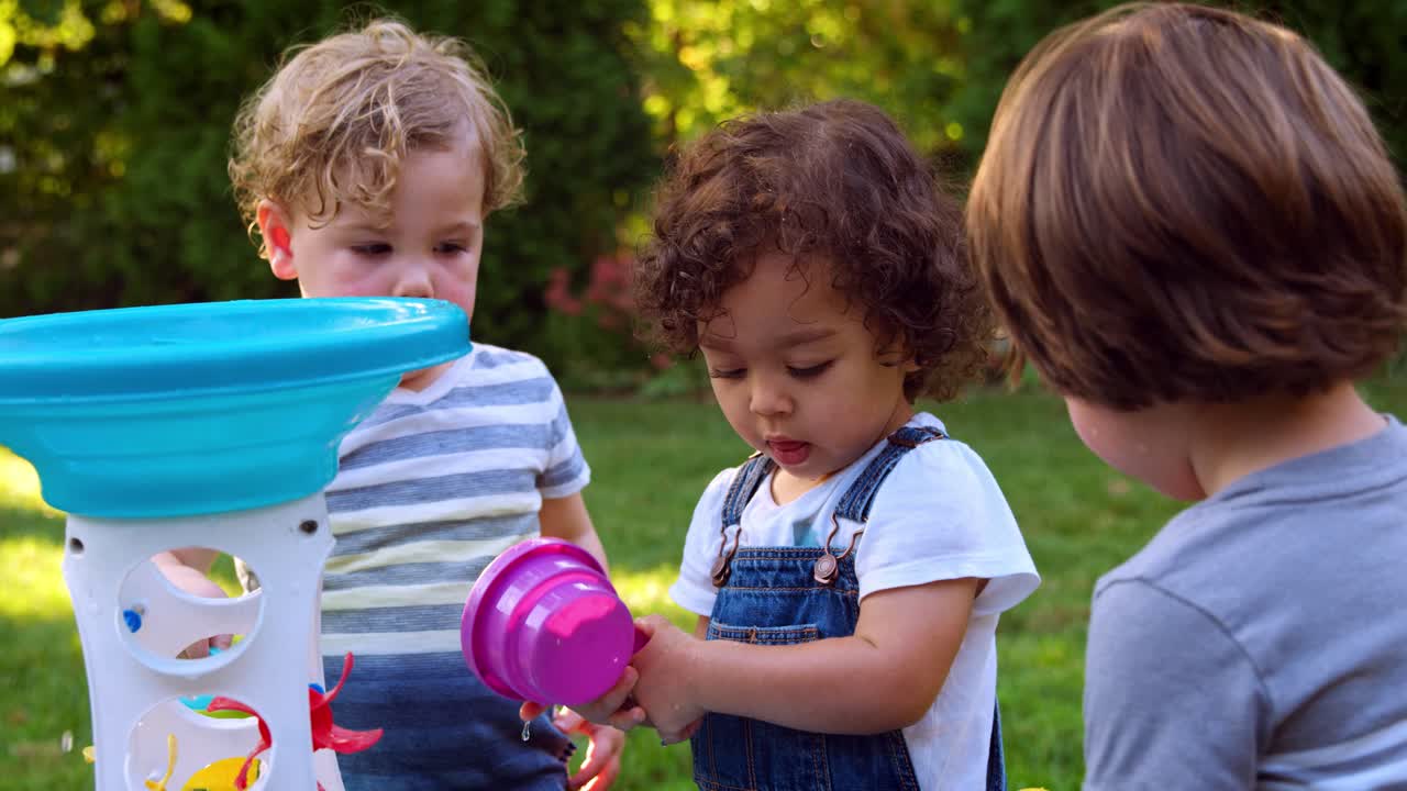 grupo de niños pequeños jugando con la mesa de agua en el jardín
